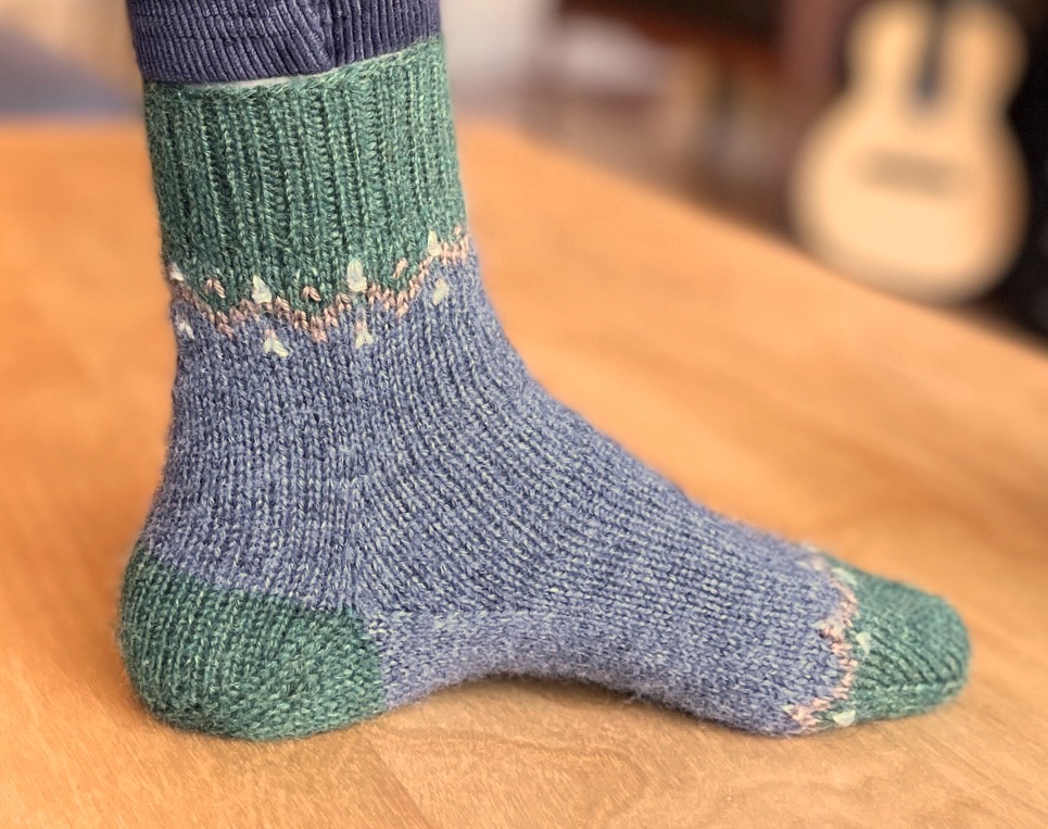 Short gray sock with green toes, heel, and cuff. Handknit from Monocot Socks patter.